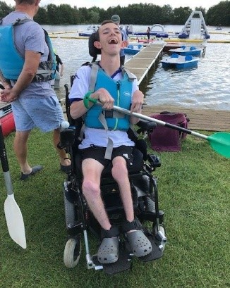 DL enjoying accessible holidays abroad. Young man in wheelchair with paddle by a river.