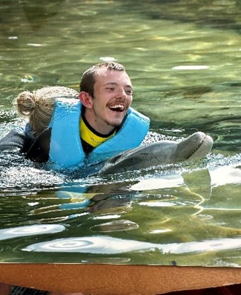 Young man on holiday, swimming with dolphin following clinical negligence compensation claims