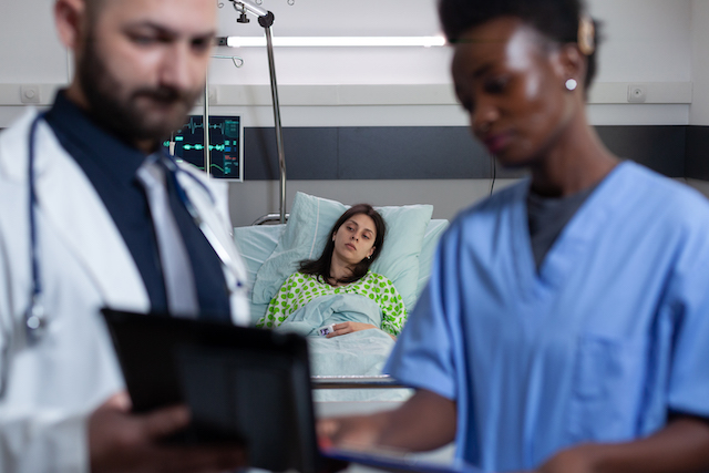 Patient on hospital bed feeling ill waiting for medic and nurse to read diagnosis from digital tablet. Highlights the human face of the Oxford maternity services report