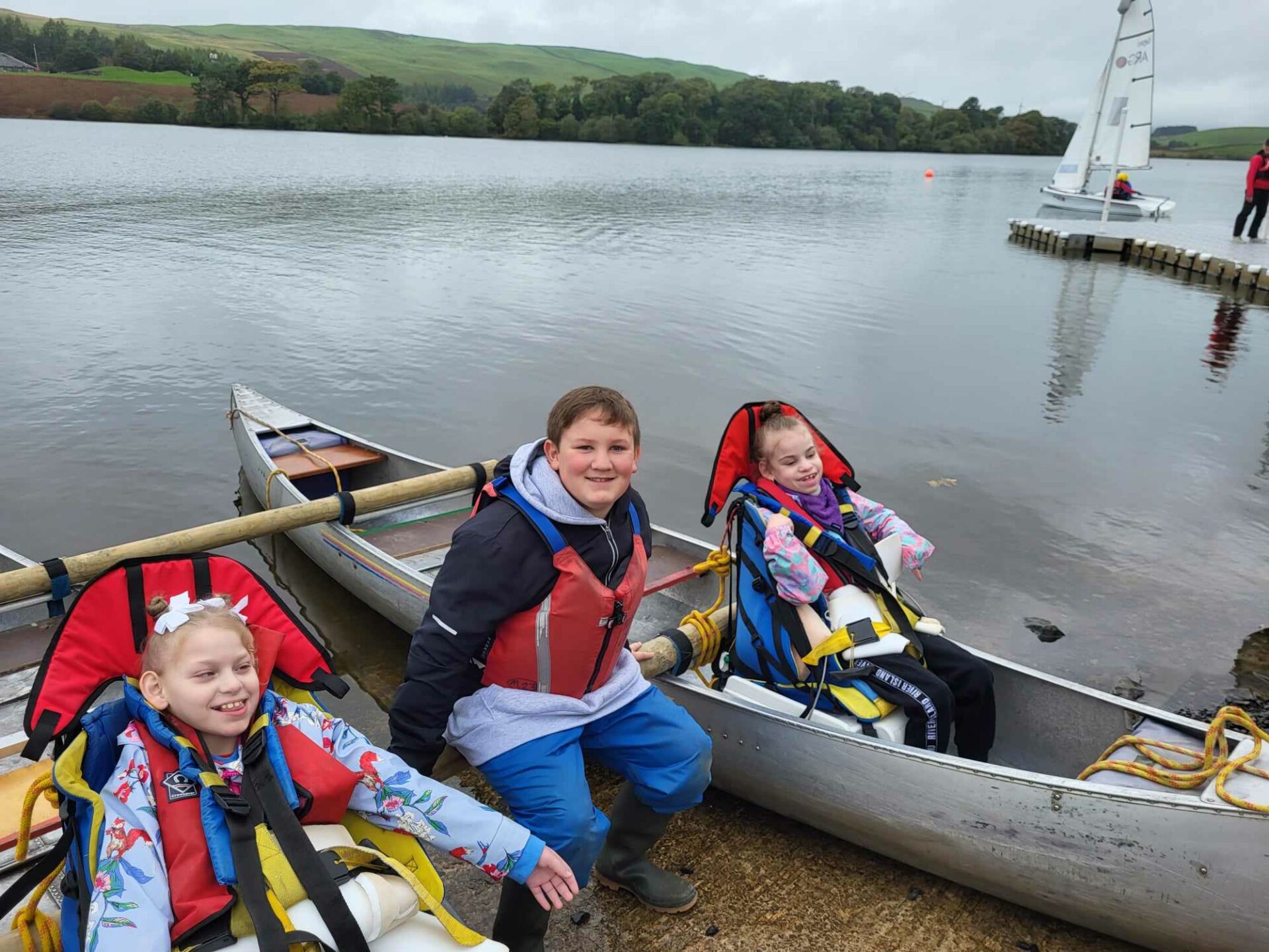 Photo of 3 children. two are in specially adapted canoes with a third child sat between the two canoes