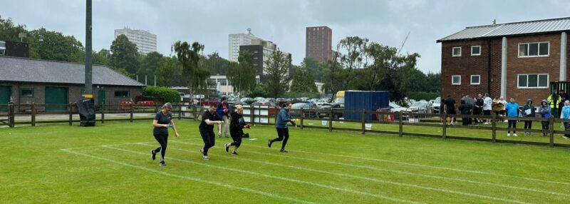 Four people running on grass taking part in an egg and spoon race