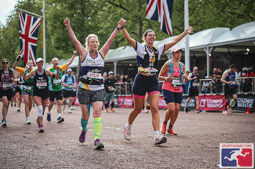 two happy female runners join hands as they celebrate crossing the finish line