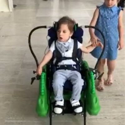 Two young children side by side, one stood beside the other in a mobility device called bugzi, part of the Pace assistive technology loan library
