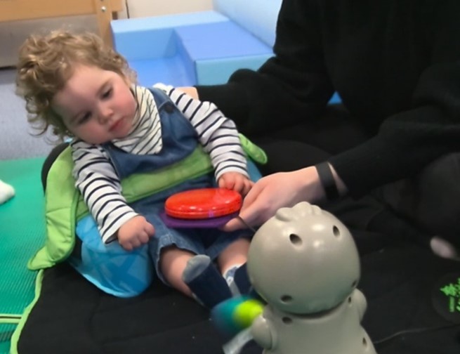 Young child in supportive seat playing with assistive technology toys