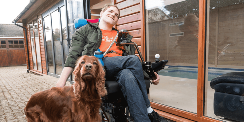 Photo of Ryan in his wheelchair with his dog beside him