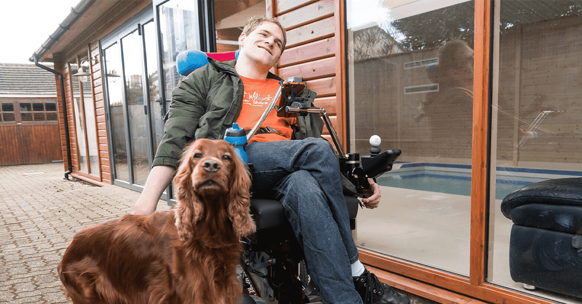 Photo of Ryan in his wheelchair with his dog beside him