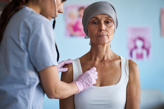 a woman whose breast cancer was misdiagnosed sits upright while a nurse performs an examination