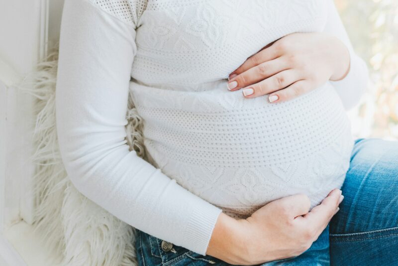 Photo of a woman in a white jumper holding her baby bump